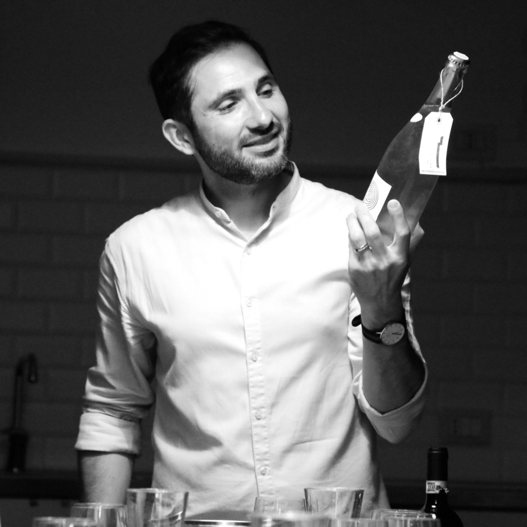The owner of VinoRoma, Maurizio Di Franco, who is holding a bottle of wine and describing it to members while leading a tasting.