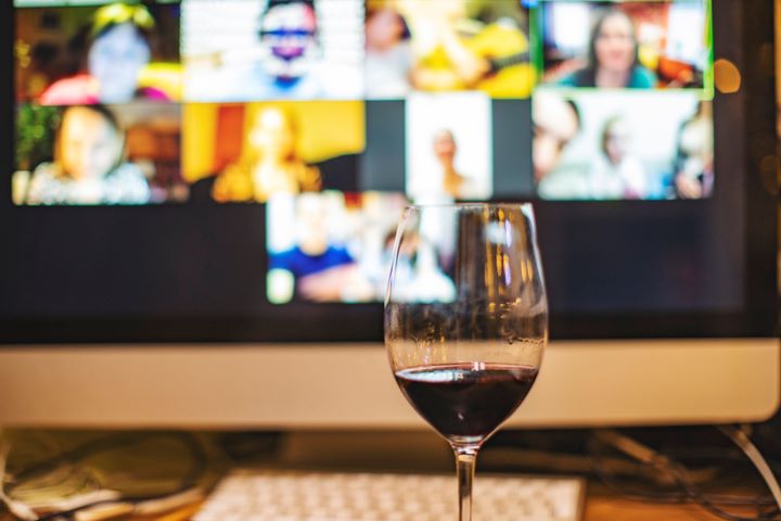 A glass full of red wine in front of a computer screen with a video call with members during a virtual tasting.