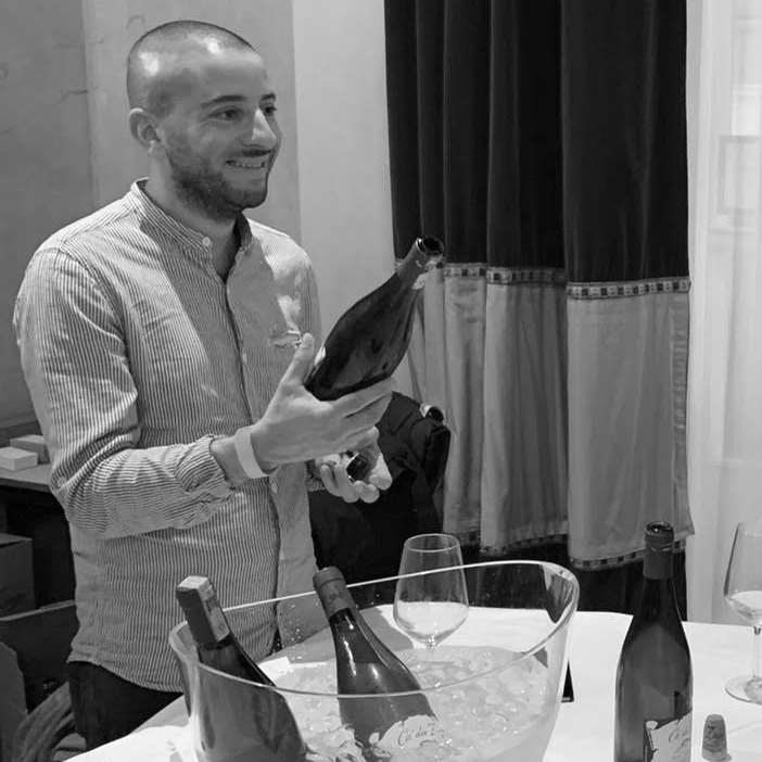 Sommelier and wine educator of VinoRoma, Frank Villani, who is holding a bottle of wine to pour to members during a tasting.