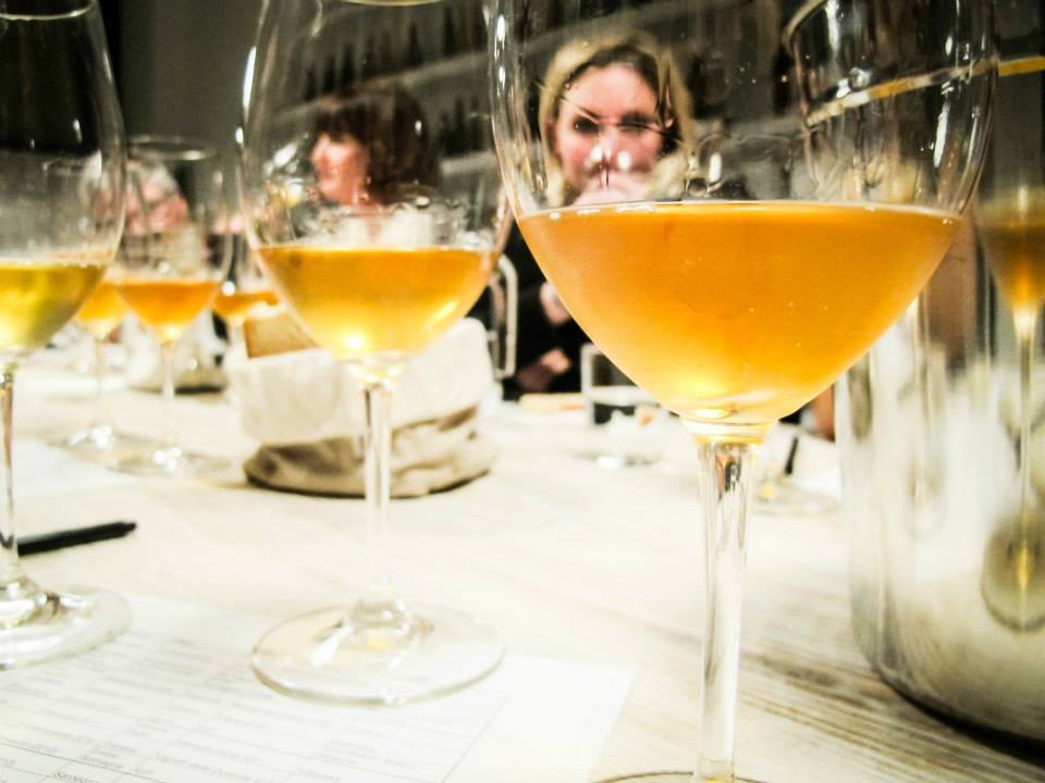Membri al tavolo di degustazione di VinoRoma che si intravedono attraverso dei bicchieri di vino bianco durante un corso di formazione.