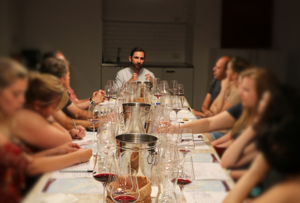Un sommelier e wine educator spiegando come degustare il vino ai membri seduti al tavolo di degustazione di VinoRoma durante una degustazione.