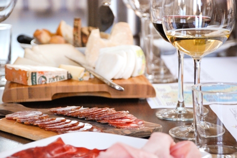 The tasting table set with cured meats, cheeses, glasses with red and white wine and printed material during a tasting.